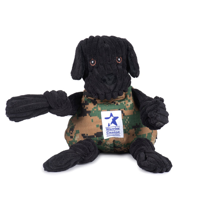 A plush black laborador toy which has a digital camo vest and Warrior Canine Connection logo patch on the chest.